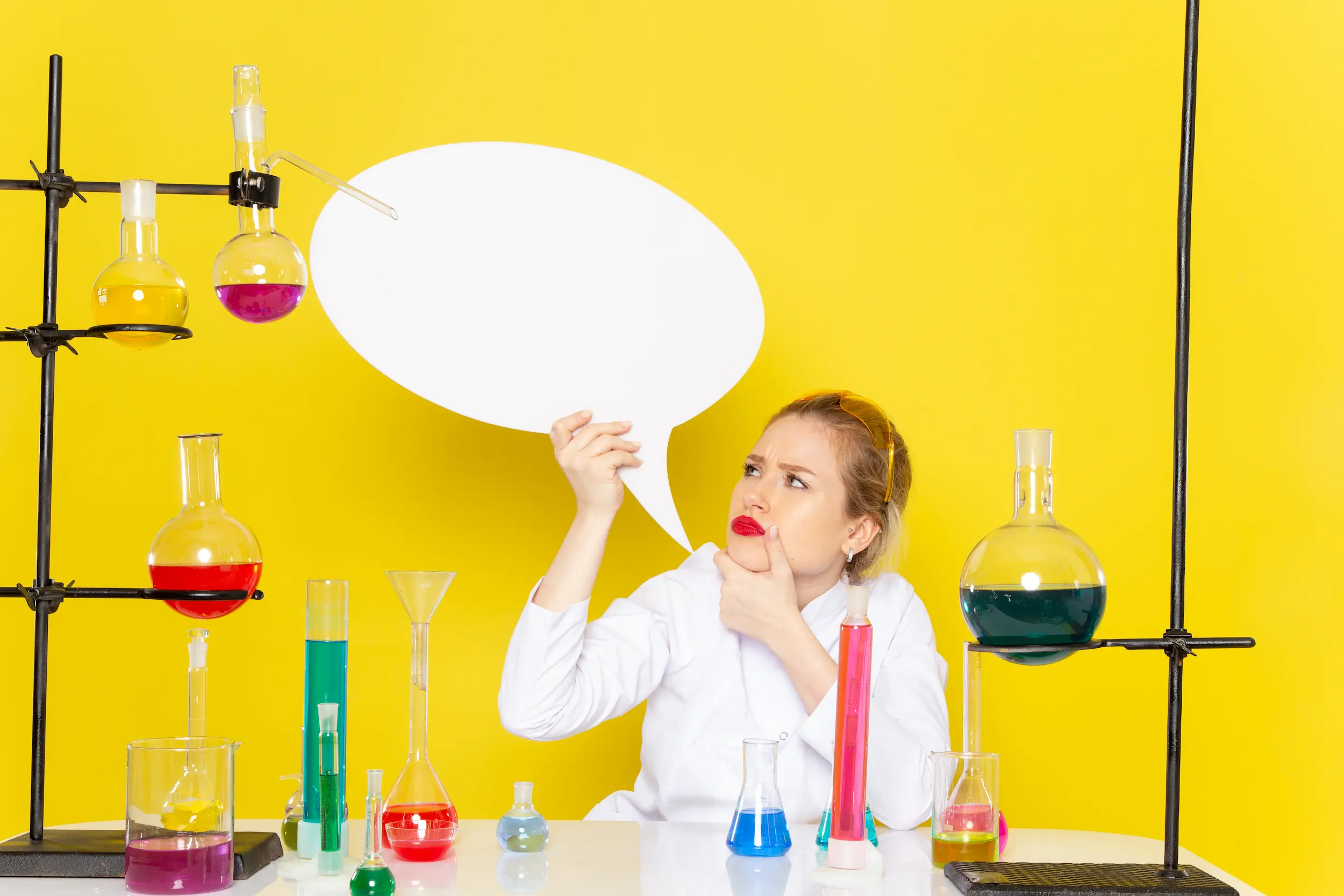 front-view-young-female-chemist-sitting-white-suit-with-different-solutions-holding-white-sign-yellow-space-chemistry-science-process-job.webp